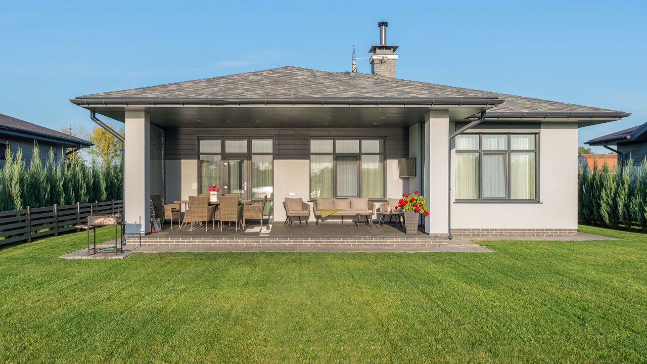 A rear yard in daylight — a covered patio, planting beds and lawn running to the fence line
