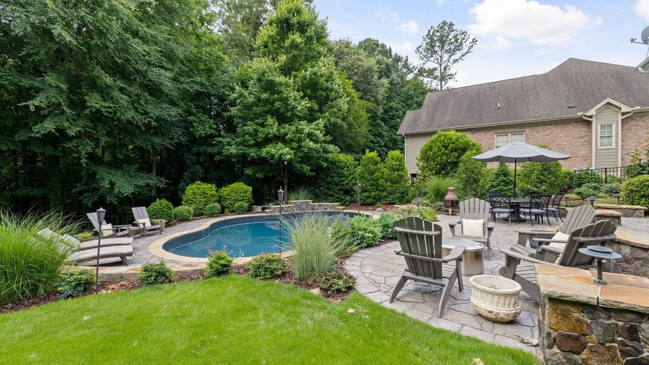 A finished rear yard in daylight — free-form pool coping, flagstone patio, a dry-stack seat wall, boulder edging, ornamental grasses and cut lawn