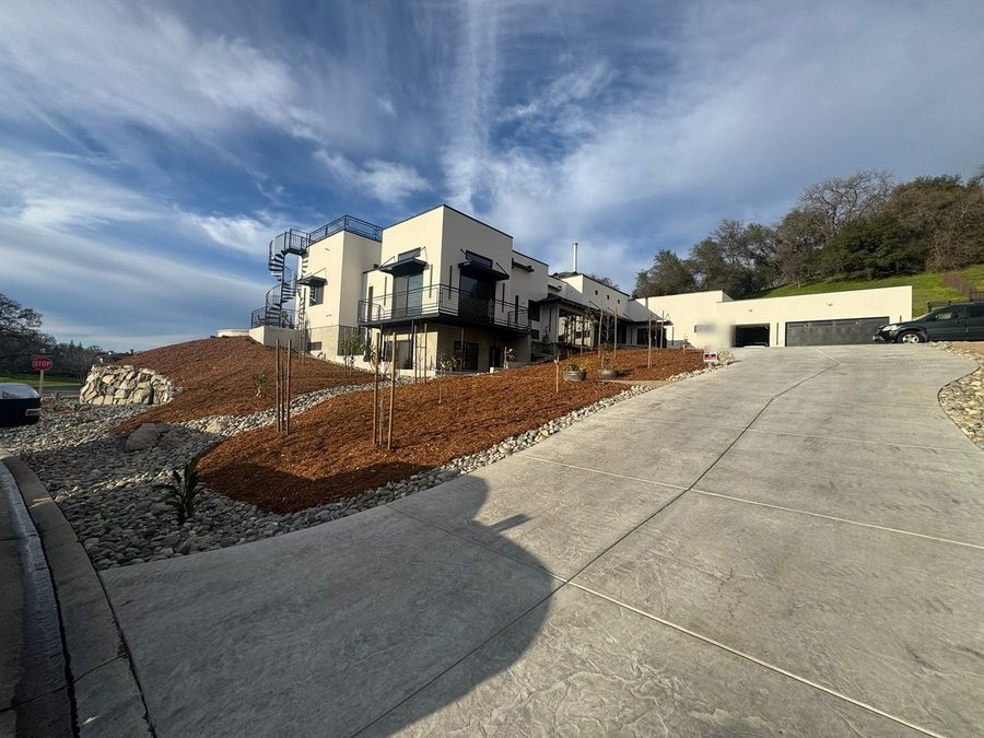 A finished frontage graded away from the buildings, with a new concrete drive and apron and bark terraces falling toward the street.